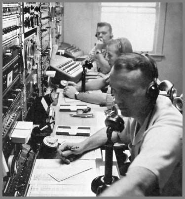 Three operators at a larger 1962 operating console.