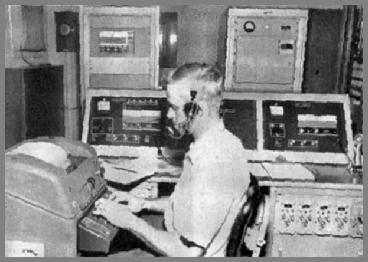 Paul Hise at the TTY with console beside him and transmitters in the background.