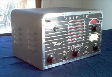 Tabletop Radio transceiver with rectangular speaker grill in the center, tuning dial window and knob on the right, 3 knobs ane 3 toggle switchea on lower front..