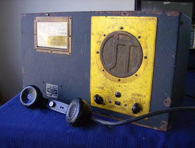 Large tabletop radio transceiver with 2 knobs below a big speaker grill on right front.