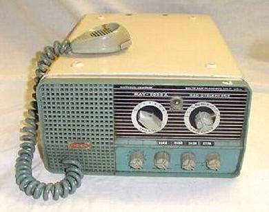 Tabletop Radio transceiver with 2 big knobs, 4 small knobs and speaker grill on left front and microphone on top of left side.