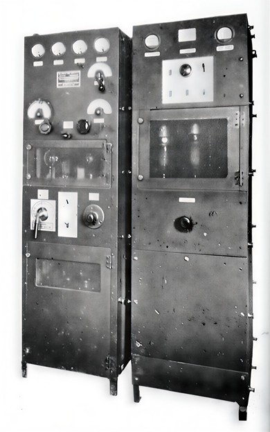 2 tall cabinets with multiple knobs and meters and large tubes showing through 3 glass windows. 
