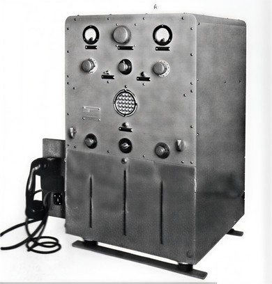 Man holding a handset and operating a 4 foot high transceiver with 3 meters, 4 knobs, a hangup loop for the handset and a speaker